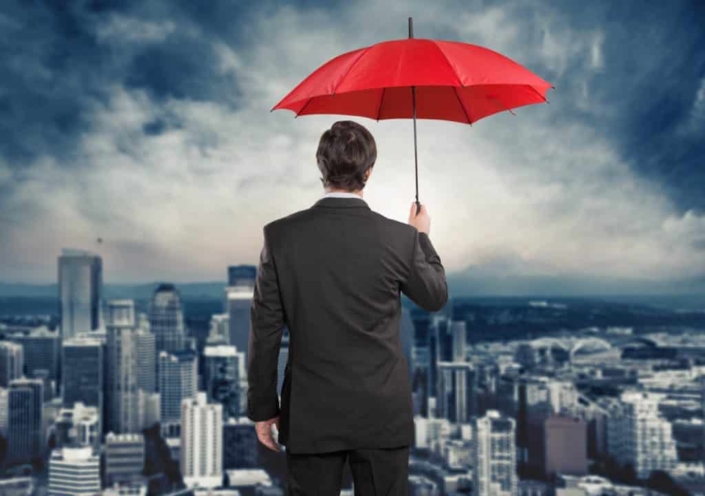 A man stands in the rain holding a red umbrella, looking over the city.