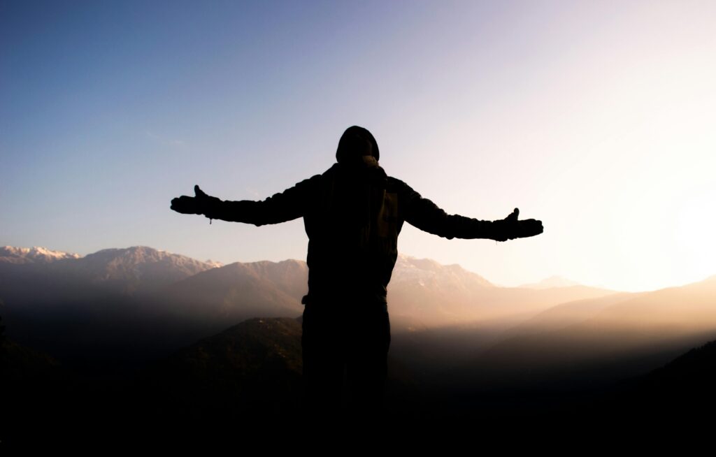 Person with arms outstretched embracing the sunrise over Indian mountains, symbolizing freedom and adventure.